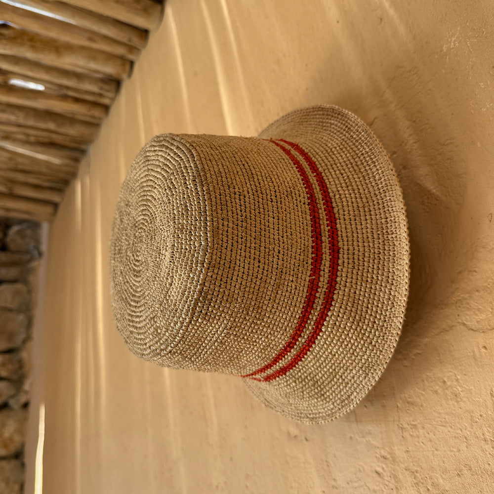 Lovelies Studio - The Marconi bucket hat, a stunning creation meticulously crafted by local artisans in Madagascar exclusively for Lovelies Studio.  Made from raffia, a natural fiber renowned for its durability and flexibility, the Marconi bucket hat is not only stylish but also eco-friendly. The raffia is carefully colored by hand using traditional methods and left to dry naturally in the warm sun, ensuring minimal environmental impact.